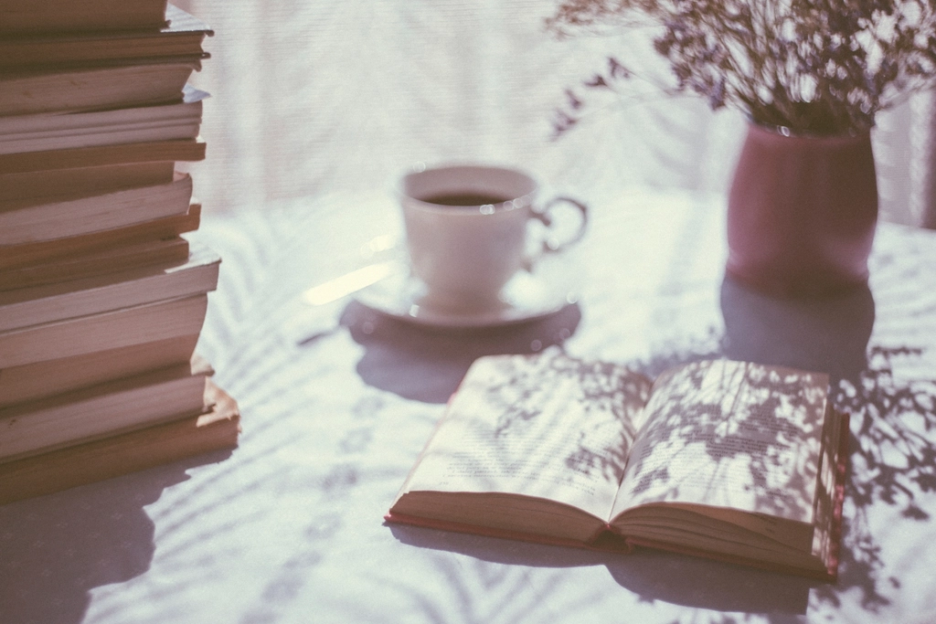 A stack of books, an open book and a cup of coffee